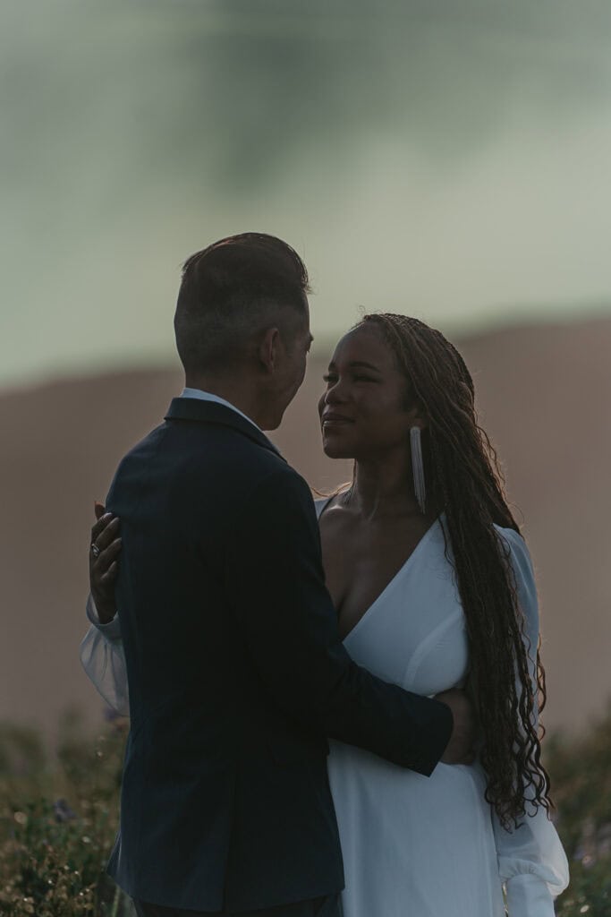 A bride and groom look into each others eyes during a foggy mountaintop sunrise.