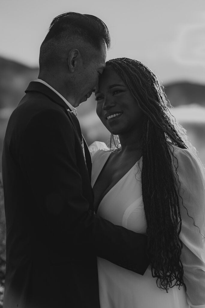 A black and white image of a bride and groom on top of a foggy mountain.