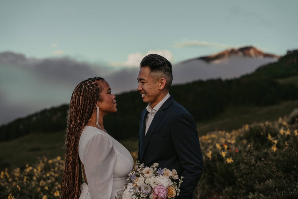 Marissa & Janiel stand facing each other on their wedding day as fog covers the mountains behind them.