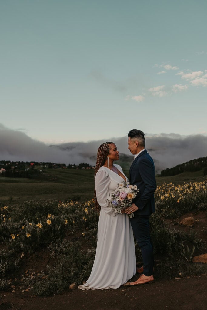 Marissa and Janiel stand facing each other on their wedding day. Mountains are in the background.