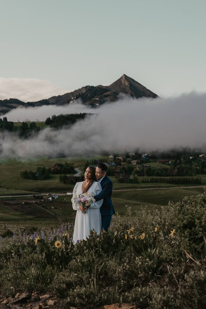 Marissa and Janiel stand in an intimate embrace as fog rolls behind them among the mountains.