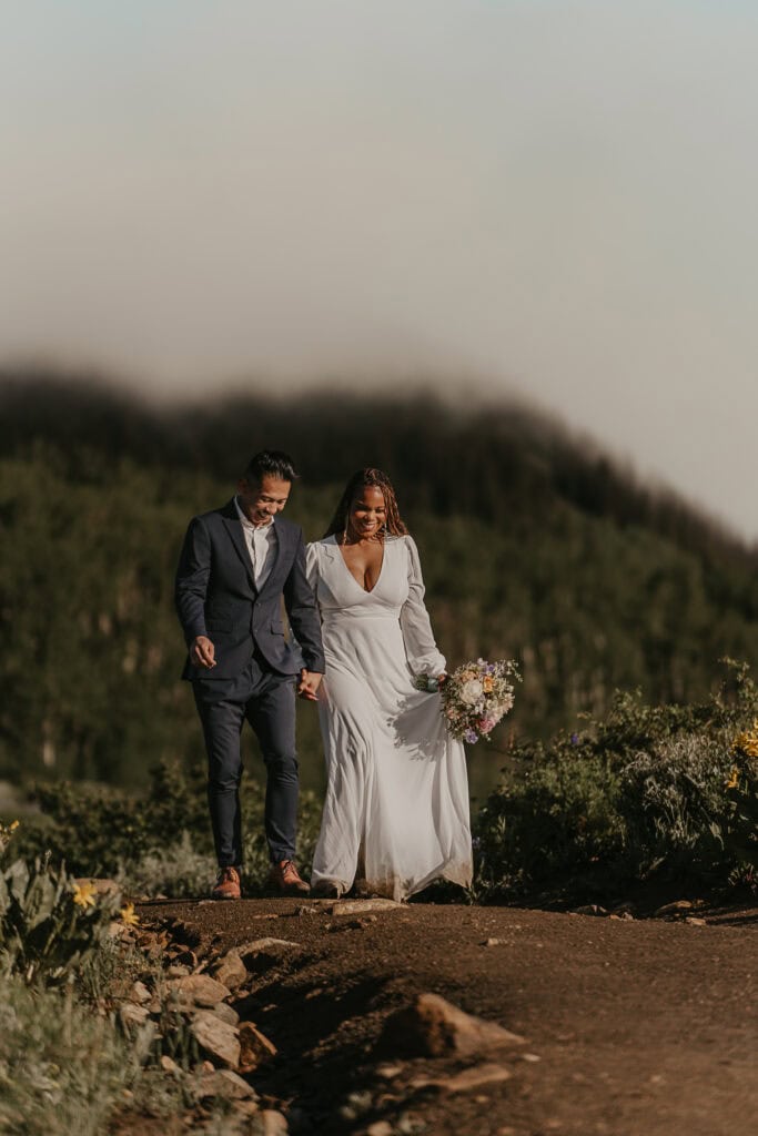 The sun shines on a bride and groom as they walk a dirt path on the foggy morning of their elopement.