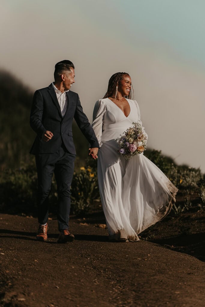 An eloping couple walks down a path of wildflowers on a foggy morning.