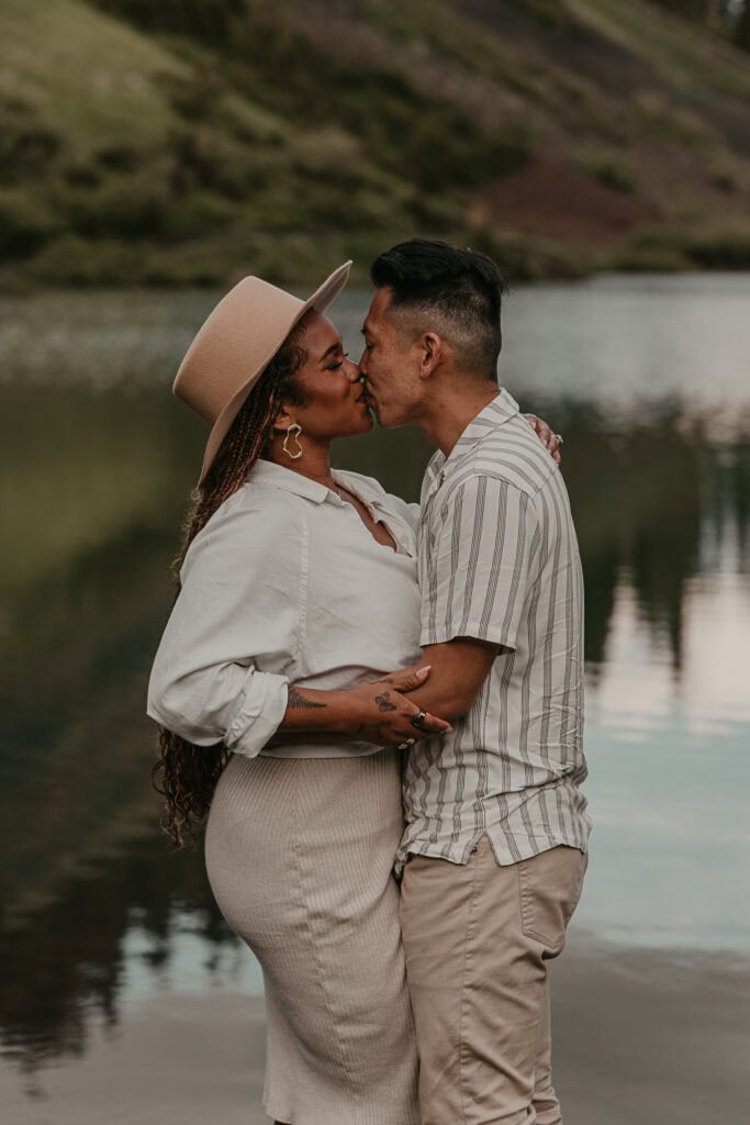 Marissa and Janiel kiss in front of a Colorado lake that reflects the mountains around them.