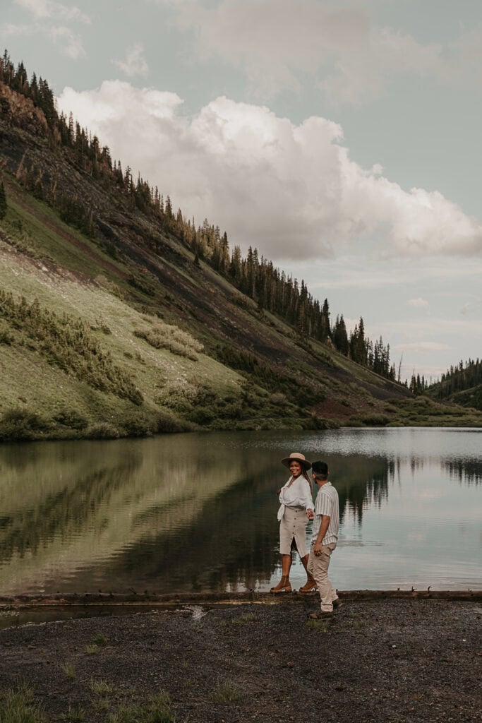 Marissa and Janiel walk in front of an alpine lake while holding hands.