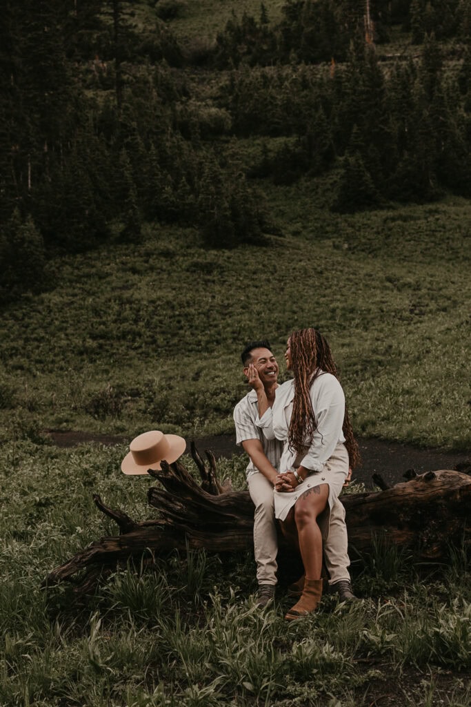 Marissa sits on Janiel's lap on a fallen log. Her hat rests on a brance.