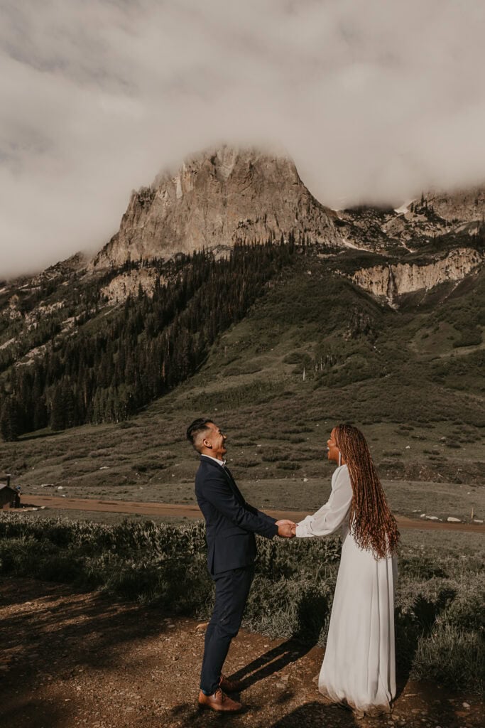 A couple laughs hysterically while saying their vows in front of a mountain.