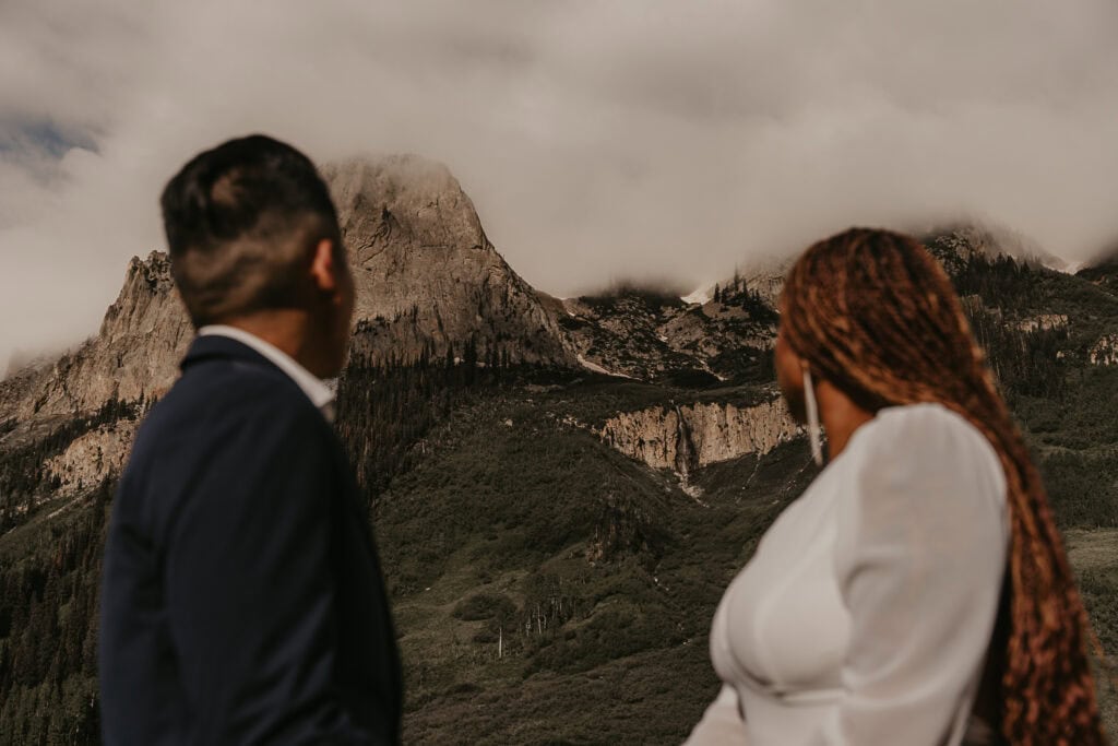 A couple looks towards a foggy mountain while holding hands during their elopement.