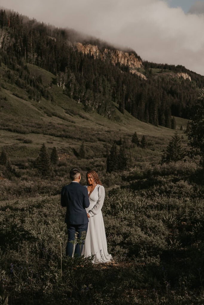 A couple exchanges vows in front of the mountains as the sun shines on them.