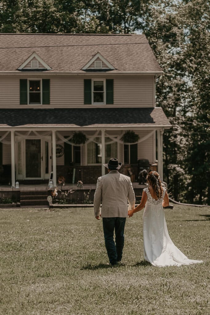 A bride and groom walk hand in hand towards their house after their backyard wedding ceremony.