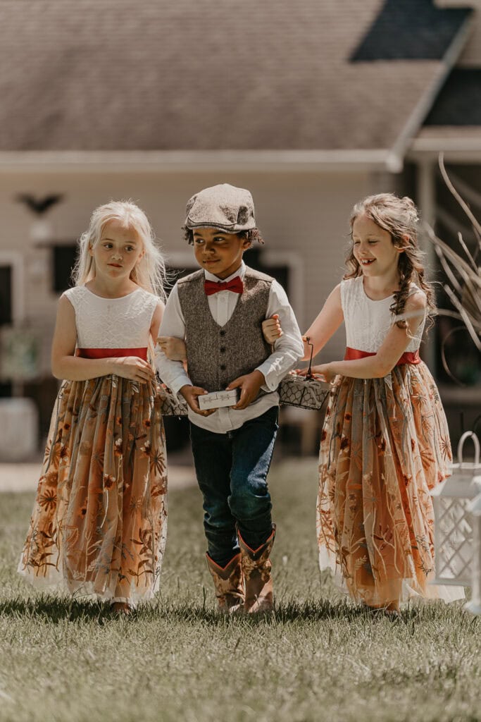 Two flower girls and a ring bearer walk down the aisle of a backyard wedding.