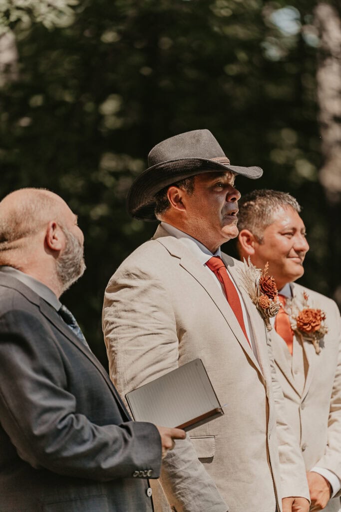 Groom is overcome with emotion, watching the bride walk down the aisle, as the minister looks at him smiling.