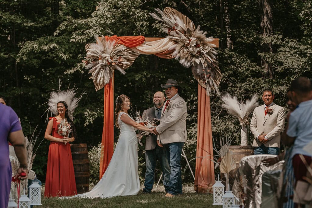 A bride and groom join hands as their outdoor ceremony begins.