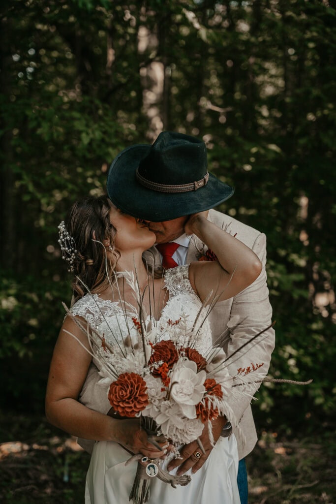 Bride and groom share a passionate kiss with his cowboy hat blocking most of their faces.