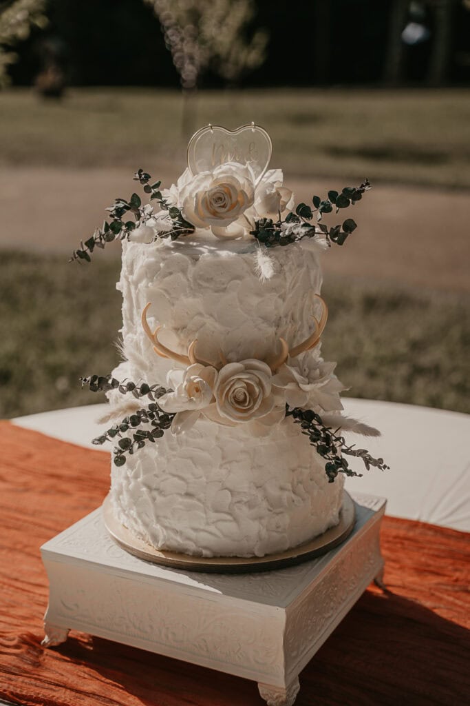 A two-tiered white wedding cake with white roses and antlers.