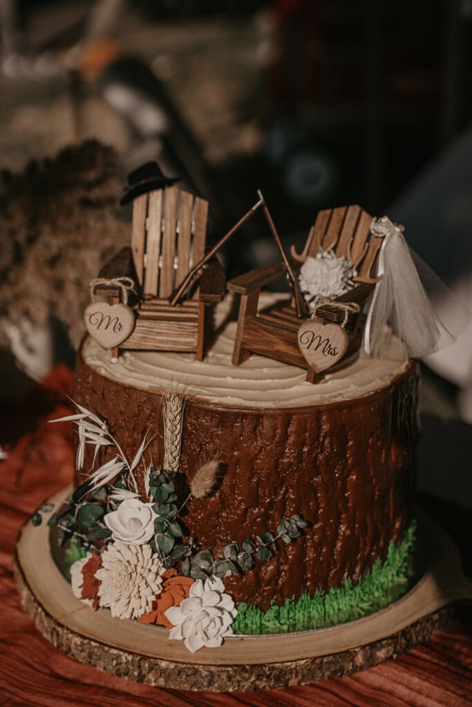 A groom's cake that looks like a log, with two chairs and rifles on the top with hearts that say Mr. and Mrs.