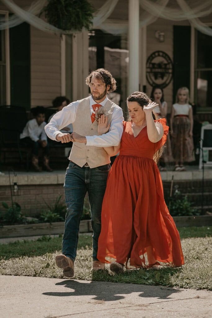 Bridesmaid and groomsman dance together outside.