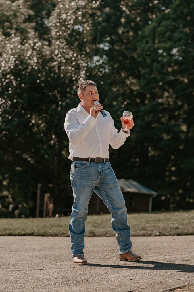 The best man toasts the bride and groom while standing outside during their reception.