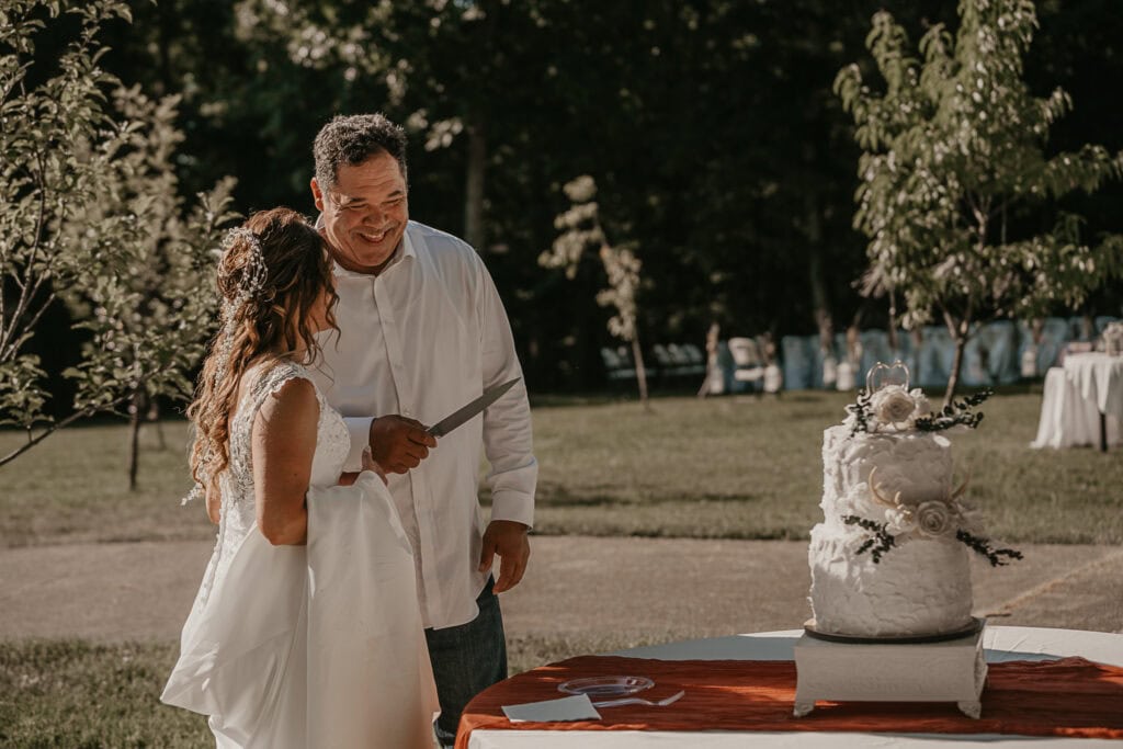 A bride and groom hold a knife, getting ready to cut their cake outside.