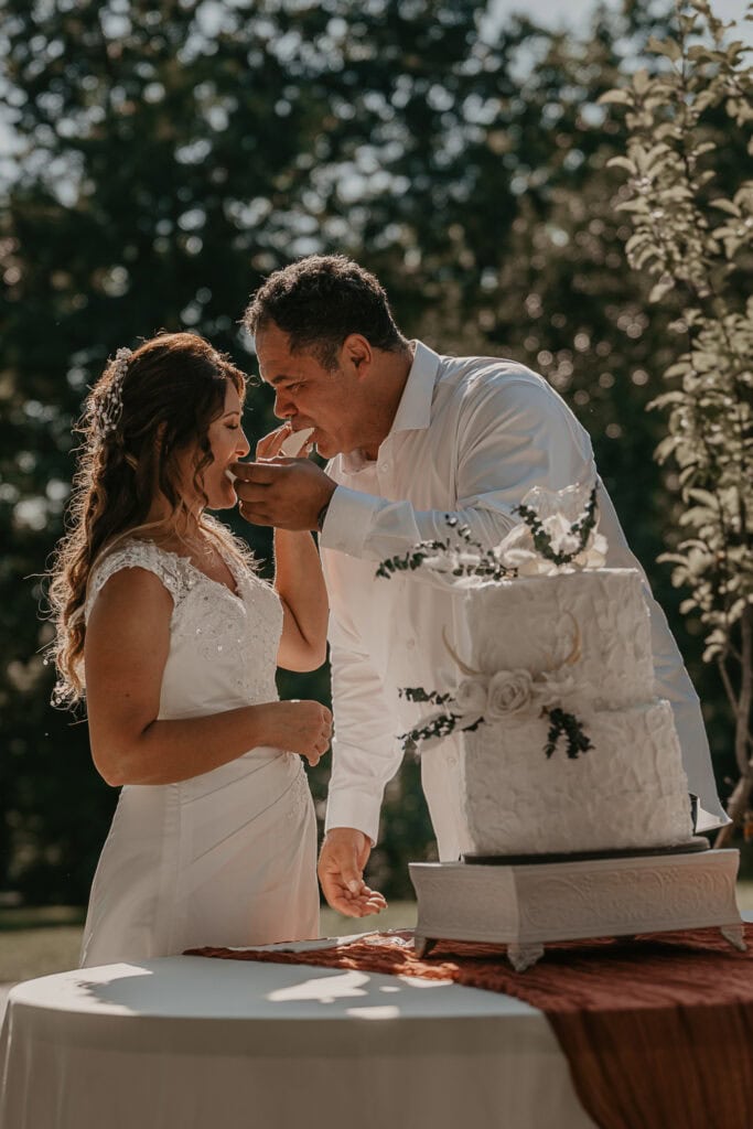 Anita and John feed each other a piece of their wedding cake as they stand outside.