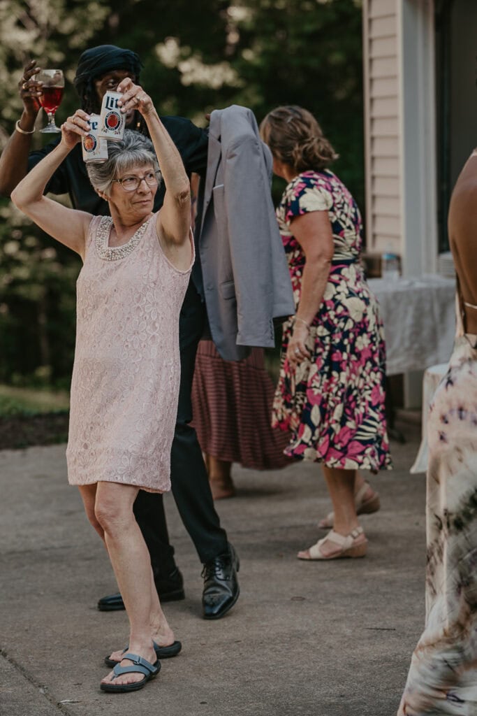 A woman holds two beers above her head while dancing on the dance floor of a reception.