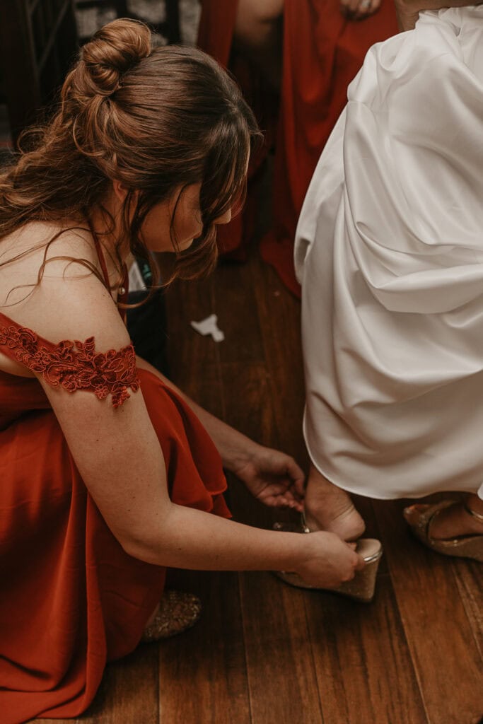 A bridesmaid helps the bride into her shoes.