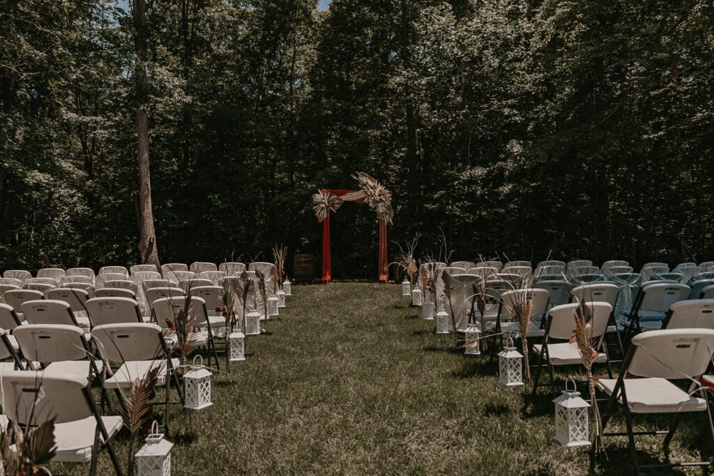 A backyard wedding setup with folding chairs and a wooden arch.