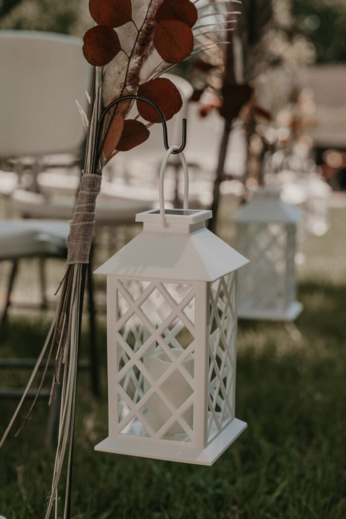 White lanterns hang alongside the aisle of an outdoor wedding.