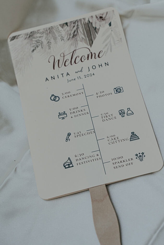 A handheld fan for an outdoor wedding that has the wedding day schedule on it.