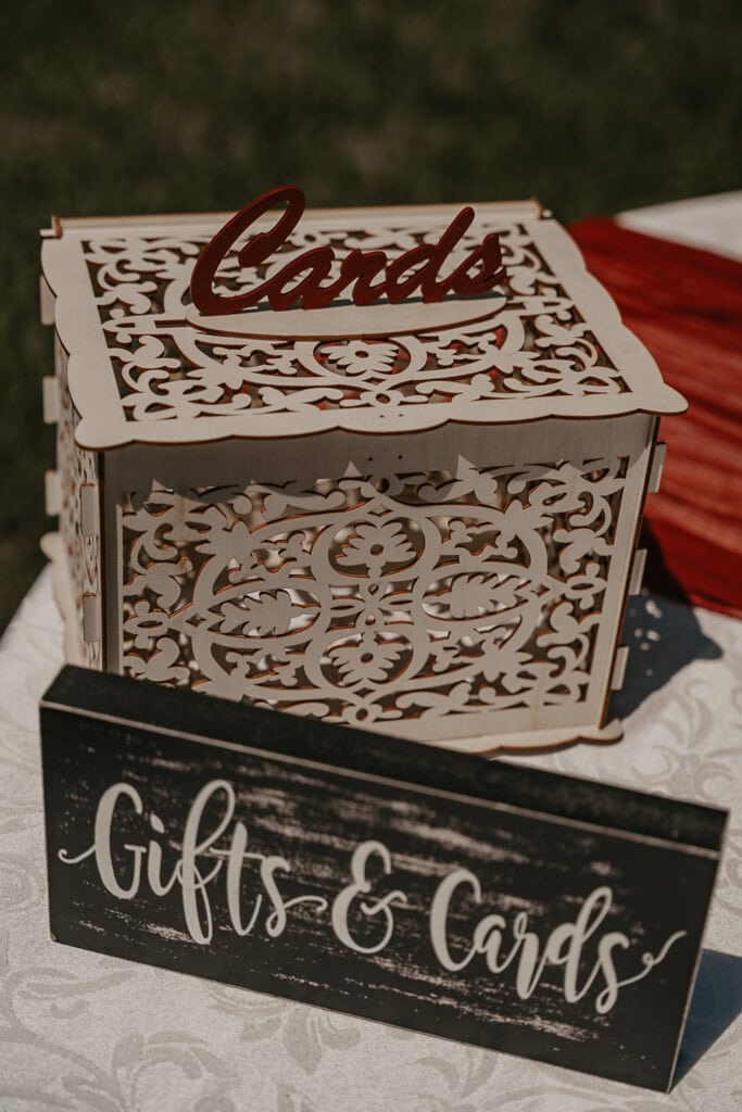 A fancy wooden box for cards on a table at an outdoor wedding with a sign that reads: gifts & cards.