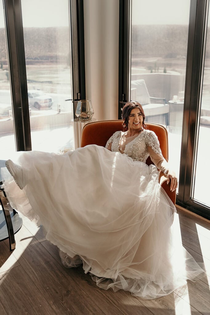 Amaris sits sideways in an orange plush chair at her Airbnb on her wedding day.