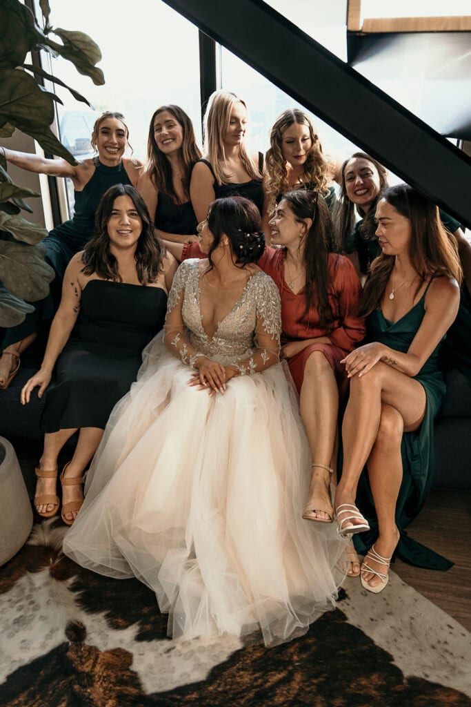 A bride and her girlfriends pose together, sitting under a stairway.