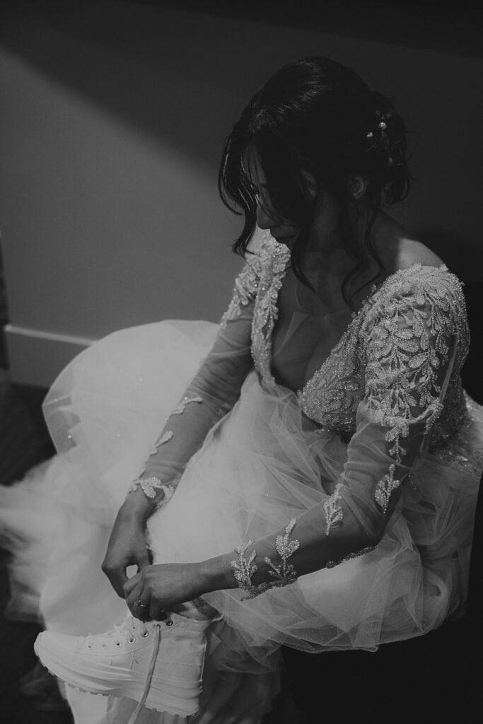 Amaris puts on high top white sneakers while wearing her wedding gown.