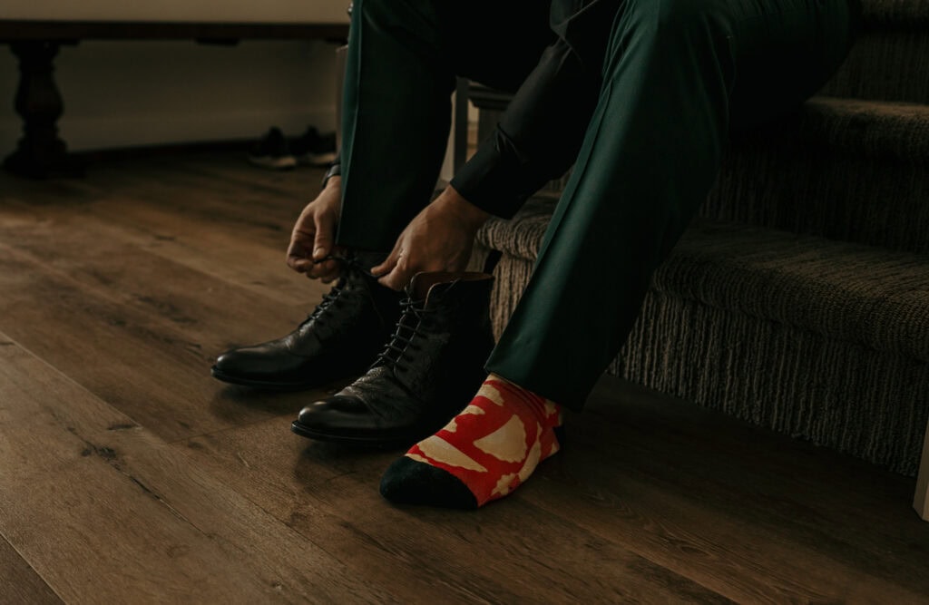 A groom wearing bright red and beige socks puts on his shoes.