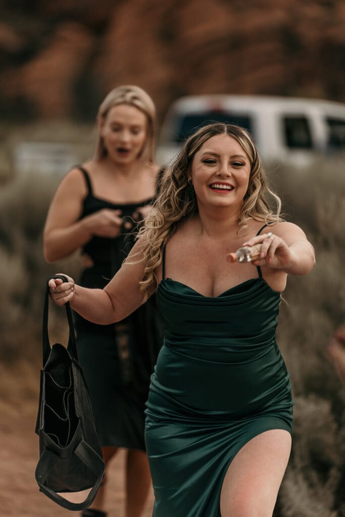 A pair of shot girls dance while handing out liqueur bottles at an outdoor wedding.