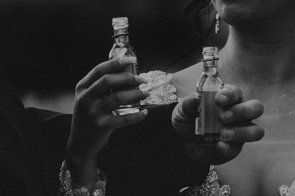 Close up of a bride and groom holding small bottles of liqueur.