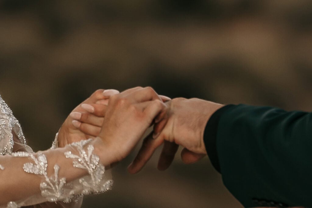 A bride places the ring on the groom's hand.