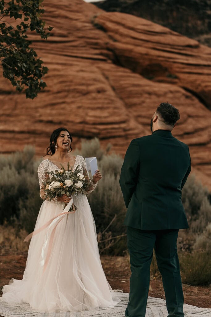 Amaris laughs while reciting her vows to Kyle. They're in front of red rocks.