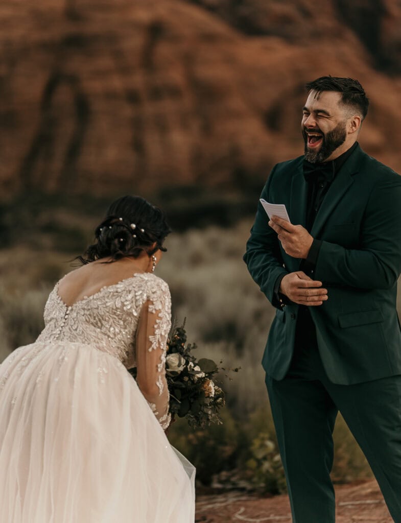 Bride and groom laugh hysterically during their vow exchange. Red rocks are in the background.