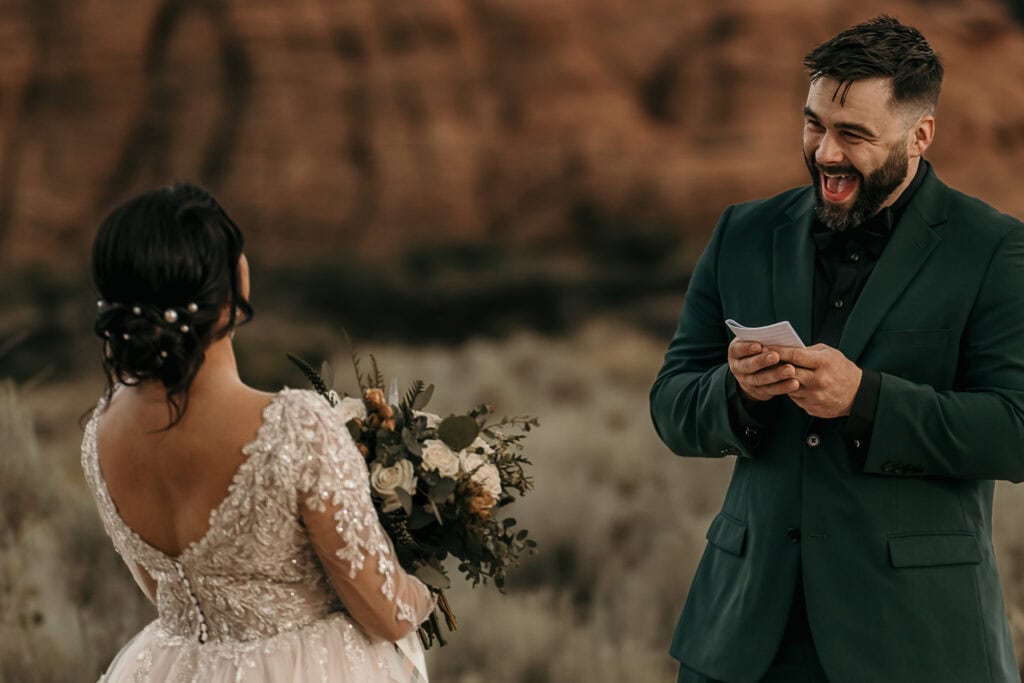 Bride and groom laugh uncontrollable while he reads his vows during their wedding.