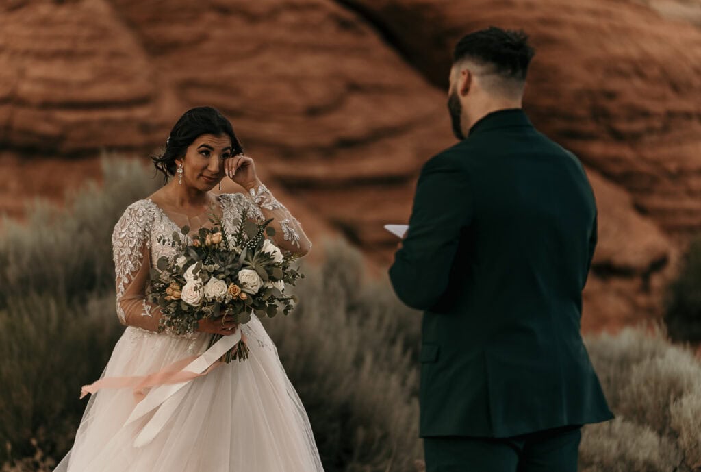 Bride wipes a tear from her eye as the groom reads his handwritten vows to her.