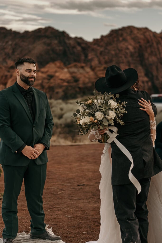 Kyle looks on as Amaris and her dad hug as her dad gives her away at their wedding.