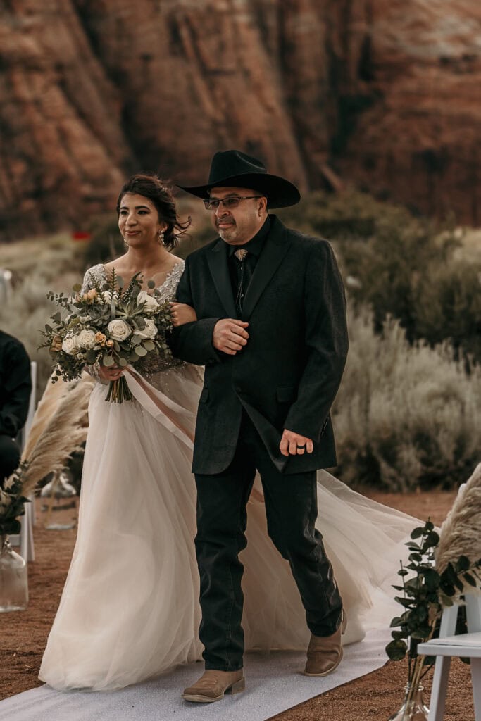 A bride and groom walk down the aisle of their Utah wedding, surrounded by red rocks.