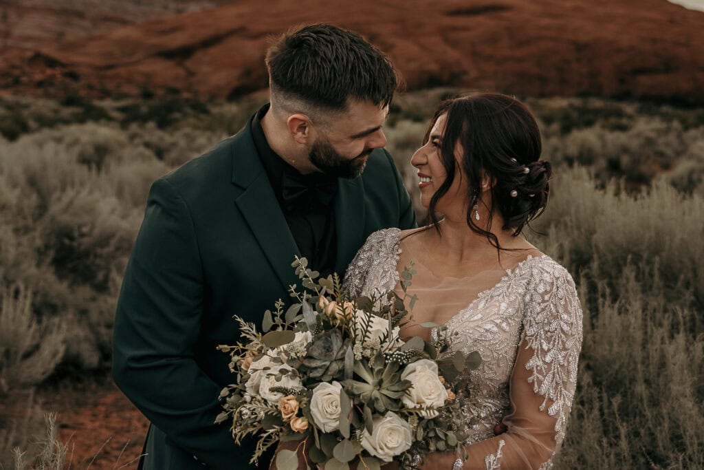 Amaris and Kyle look at each other while standing in front of red rocks,