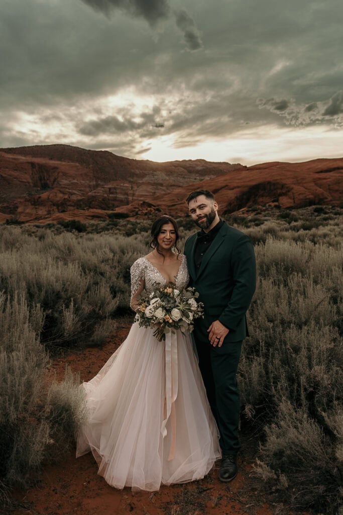 Bride and groom pose after their wedding. The sun is setting behind them and they're surrounded by red rocks.