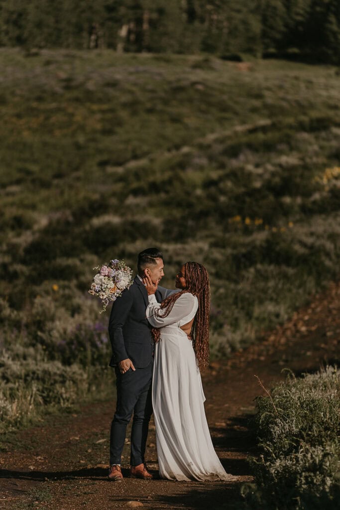 an elopement couple gazing lovingly into each others eyes on a dirt path surrounded by a lush field