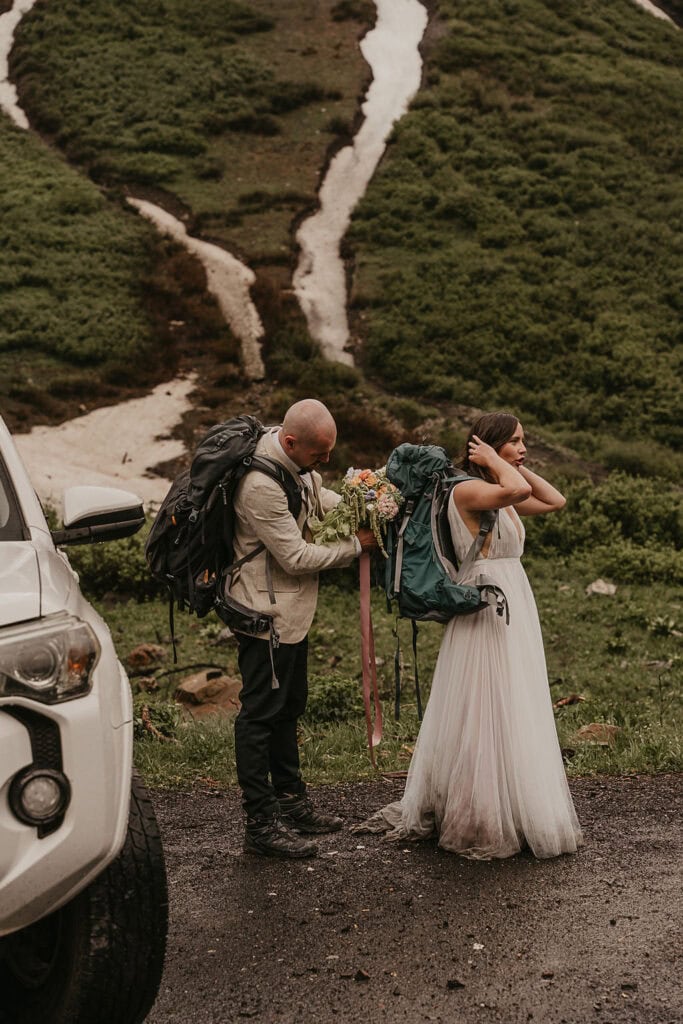 groom helping his bride put on a backpack ahead of their hiking elopement in Crested Butte