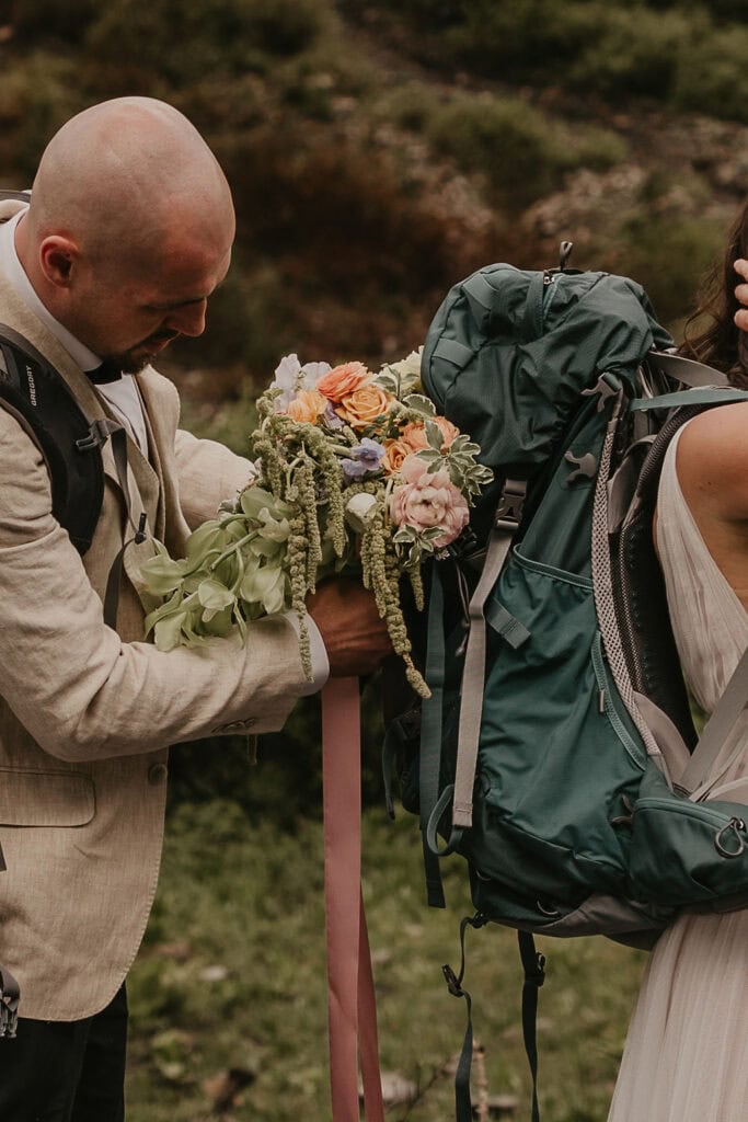 groom helping his bride put on a backpack ahead of their hiking elopement in Crested Butte