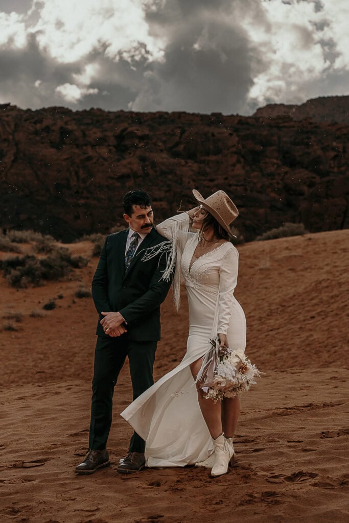 A boho bride rests her elbow on her grooms shoulder while they stand on sand dunes.