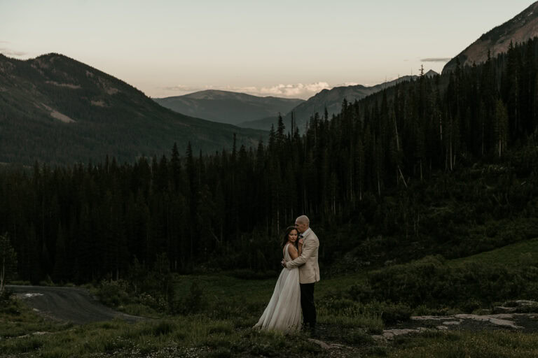 A bride and groom embrace during sunset in the mountains.